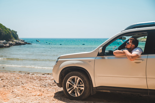 happy smiling man sitting in car at the seaside summer time vacation concept