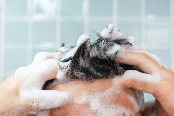 las manos masculinas se lavan el cabello con champú y espuma sobre fondo azul, vista frontal. - shampoo fotografías e imágenes de stock