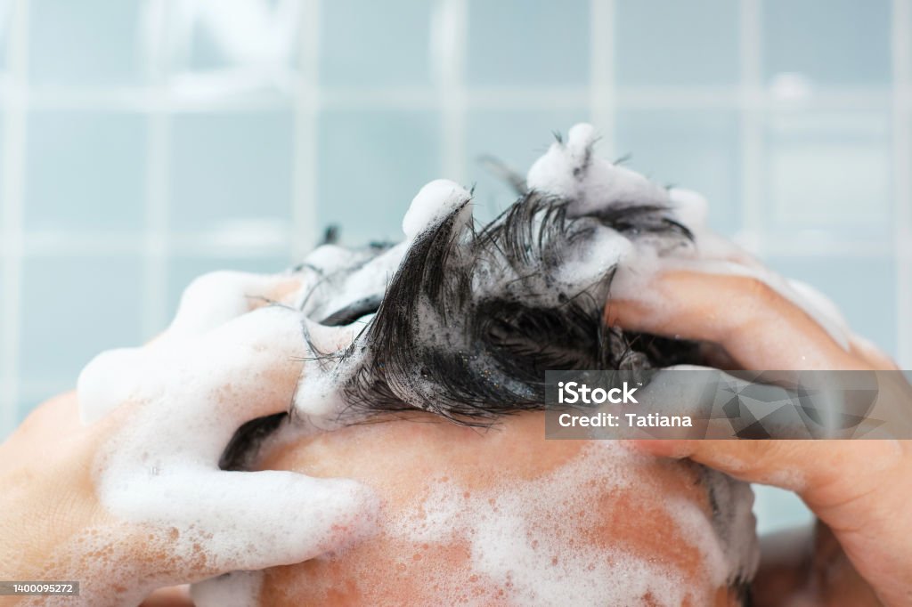 Male hands wash their hair with shampoo and foam on blue background, front view. Male hands wash their hair with shampoo and foam on a blue background, front view. Shampoo Stock Photo