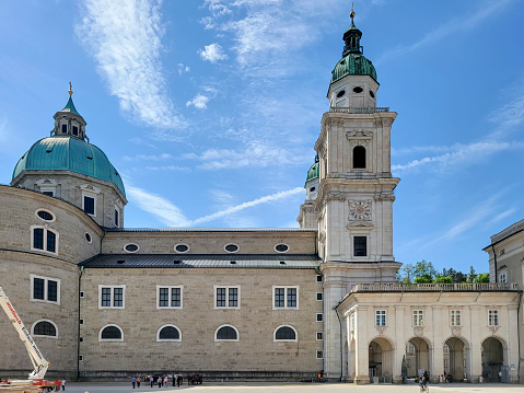 The dome and clock and bell towers of Salzburg Cathedral, Austria.  There are tourist sin the foreground and a cherry picker being used to clean a fountain statue.
