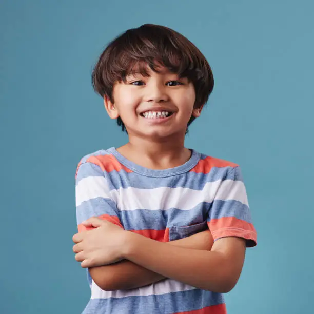 Photo of Portrait of a cute little asian boy wearing casual clothes while smiling and looking excited. Child standing against a blue studio background. Adorable happy little boy safe and alone