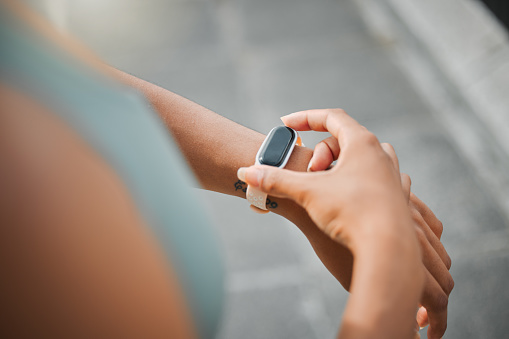 Cropped view of a fit female athlete checking the time and pulse on her watch to track her progress while taking a break from working out in the city