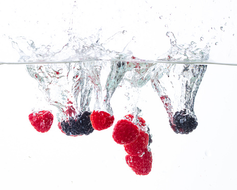 raspberries and blackberries fall into the water on a white background