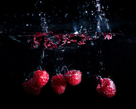 raspberries fall into the water on a black background
