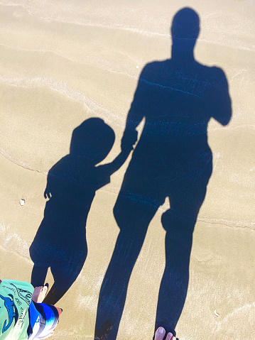 Shadows of father and son on the beach sand holding hands.