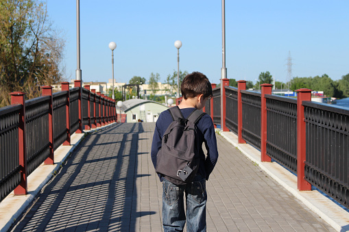 A young man with a backpack walks on a bridge on a clear sunny day