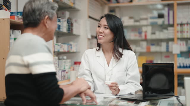 asian chinese female pharmacist explaining to senior man customer at pharmacy counter