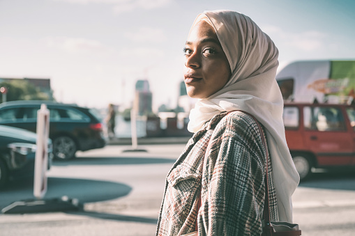 portrait of young woman with hijab on street in Berlin at sunny late summer day, turning to camera