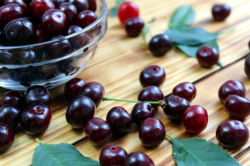 Ripe juicy cherries lie in a glass plate and on the table.