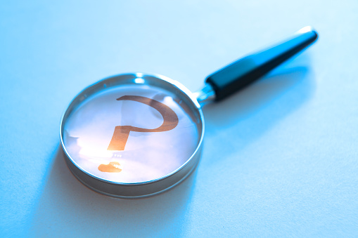 A magnifying glass rests on top of a question mark. Photographed with a very shallow depth of field.