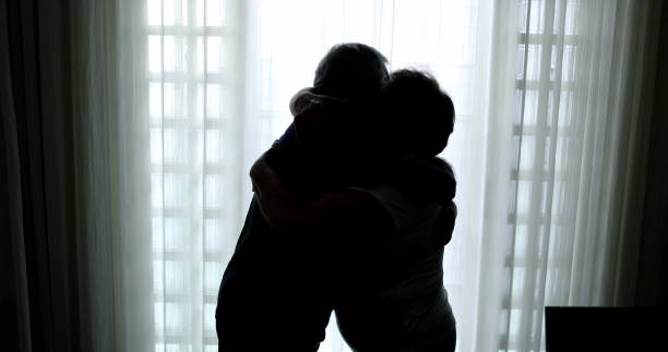 Senior couple embrace by window Senior couple embrace by window conflict in bedroom silhouette stock pictures, royalty-free photos & images