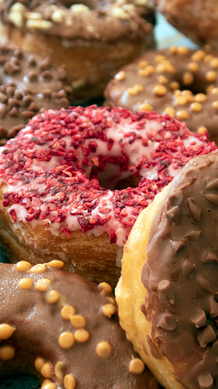 Stock photo showing close-up, elevated view of a display of croissant-doughnuts glazed with chocolate or strawberry fondant icing covered in sprinkles on a blue background.