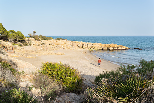 Young man walking on a idyllic mediterranean beach at sunset. Azahar Coast. Spain