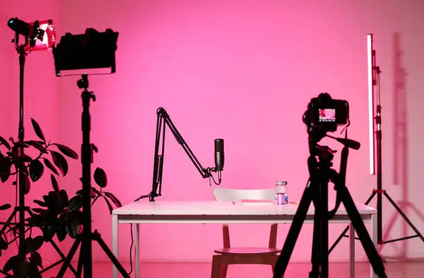 Horizontal no people interior shot of modern influencers studio equipped with camera, microphone and lighting devices, pink neon light