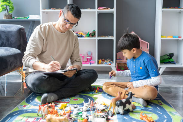 Adult with clipboard and child on the floor with toys and other objects