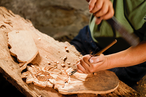 Senior disability woodcarver sitting on the ground in his studio to carve creation