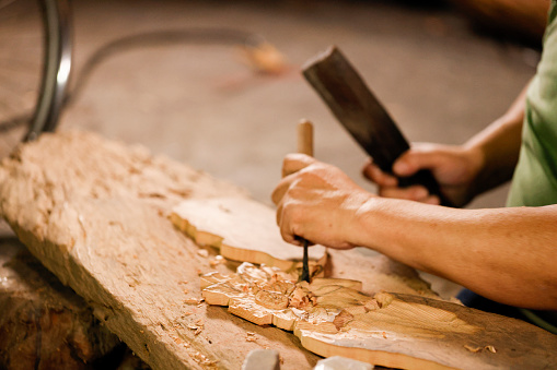 Senior disability woodcarver sitting on the ground in his studio to carve creation