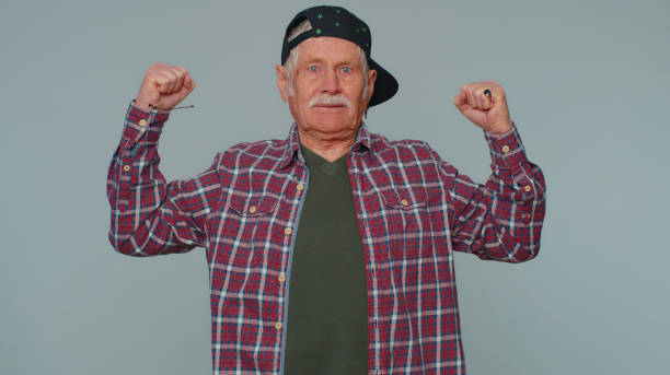 I am strong and independent. Elderly man showing biceps, looking confident, feeling power strength to fight for rights, energy to gain success win. Grandfather isolated on gray studio wall background