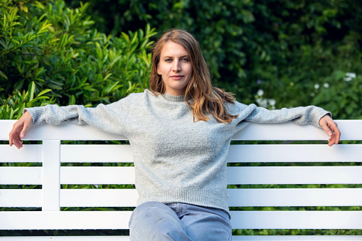 portrait of blond woman sitting outdoors in park on white bench