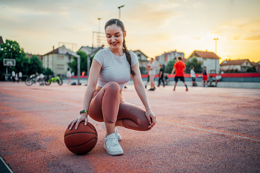 Young smiling woman with a basketball in an outdoor court