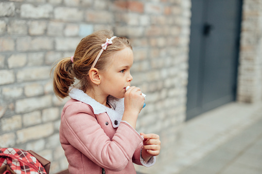 Adorable preschool girl applying lip balm outdoors