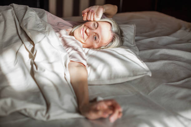 istock Happy middle aged woman sits on bed and stretching arms 1400111705