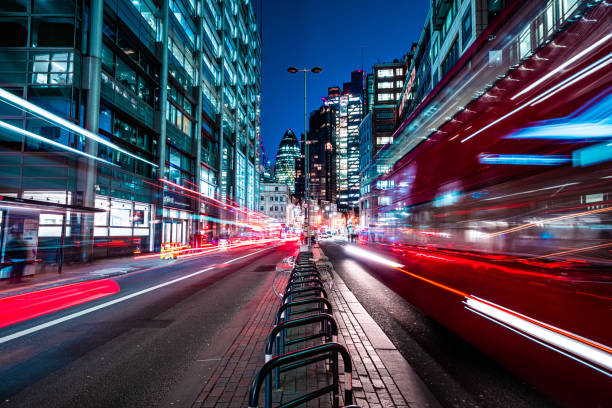 autobus rossi di londra che sfrecciano attraverso la strada notturna dei grattacieli della città - esposizione via foto e immagini stock