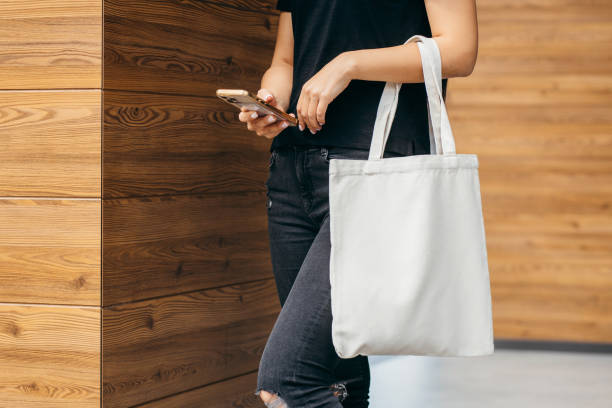 joven modelo en la calle sosteniendo una bolsa ecológica blanca y un teléfono móvil
, maqueta - tienda de telas fotografías e imágenes de stock