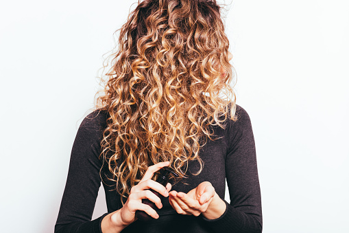 Young woman holding cosmetic oil applying on her curly hair to prevent split ends