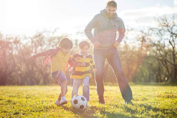 istock Two young boys playing soccer with father at public park at sunset 1400116231