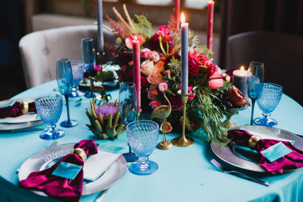 Table setting at the wedding reception. Floral compositions with beautiful flowers and greenery, candles, laying and plates on a decorated table.