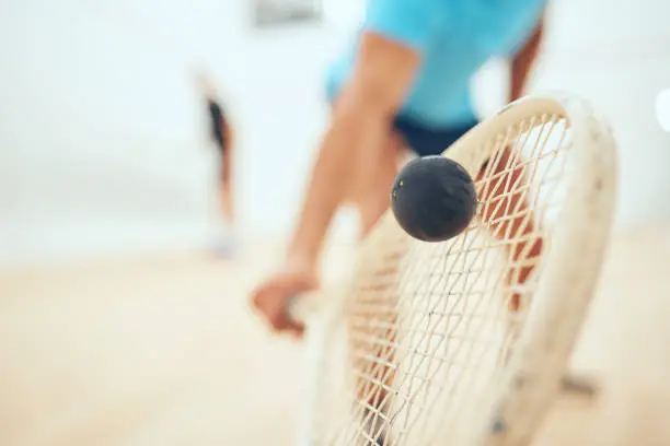 Photo of Closeup of unknown athletic squash player using a racket to hit a ball during a court game. Fit active mixed race male athlete training and playing in a sports centre. Healthy cardio and motion blur