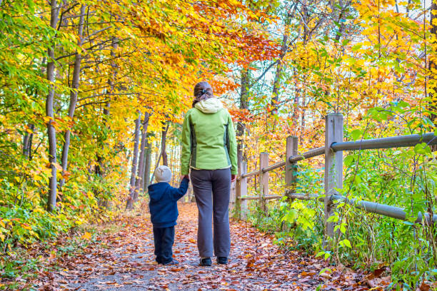 Mother walks with small child in a forest during autumn.