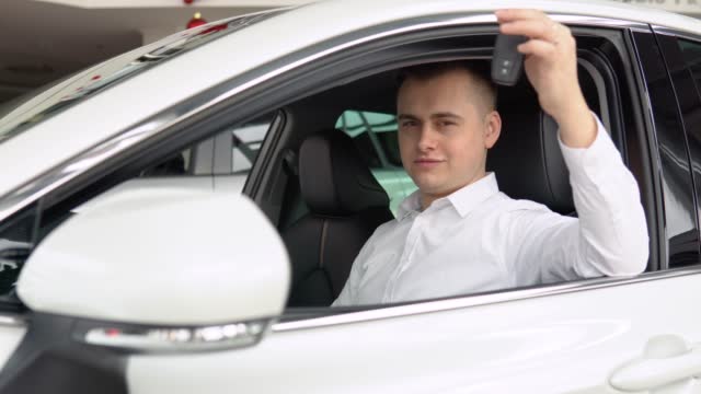 Happy stylish man showing keys of his new car in dealership. Auto business, car sale