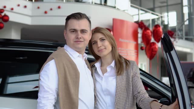 Happy couple at a car dealership with a new car in the background
