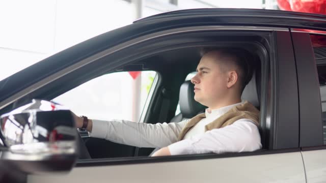 Portrait of a young confident man sitting in a new car at a car dealership