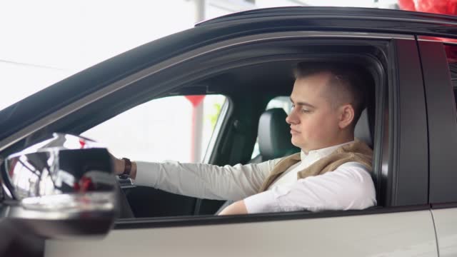 Portrait of a young confident man sitting in a new car at a car dealership. Stylish man inspects a new car at a car dealership