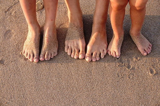 Three pairs of feet on the sand. Family on vacations. Feet and the grains of sand.