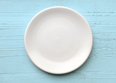 empty white plate on blue wood background, top view