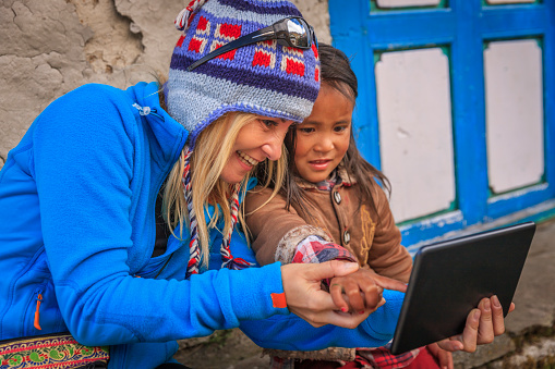 A young woman shows a little girl how to use a digital table, Nepal