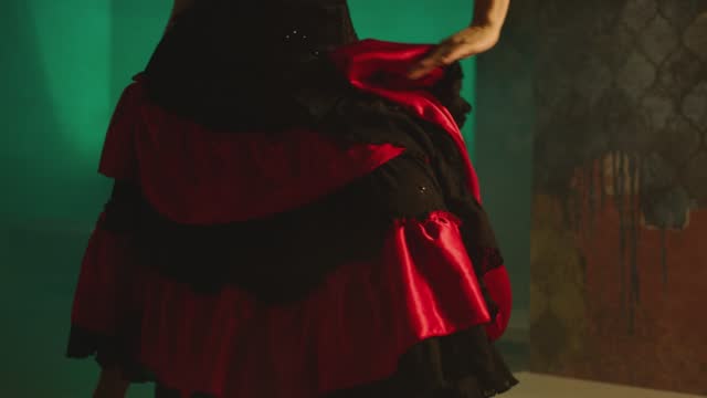 Woman dancing spanish hot dance . Professional dancer in latin dress performs dance movement by skirt . Closeup studio shot of female artist dancing inside dark place . Concept footage of dance art