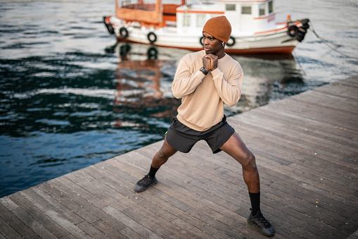 A young black man doing stretching exercises, he is by the sea and enjoys beautiful Istanbul while training outside.