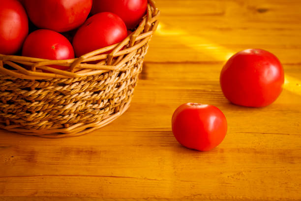Ripe juicy red tomato close-up on a wooden table against the background of a basket with a harvest of tomatoes