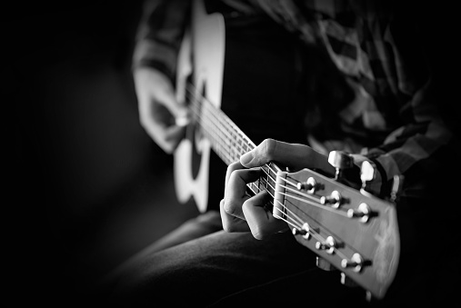 Guitar playing. A young man plays the acoustic guitar. Black and white closeup Photography.