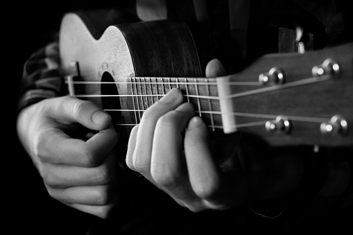 Close up of man hand playing ukulele guitar. Black and white closeup Photography.