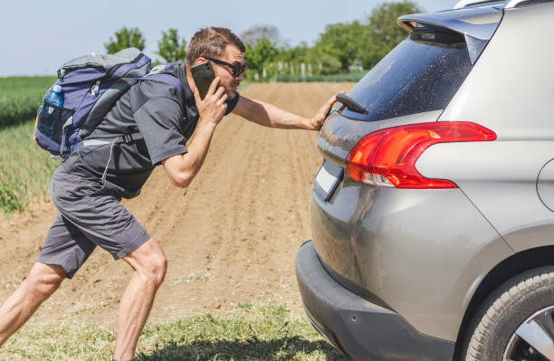 Man with backpack pushing car and calling on mobile phone. Man and his broken car. man pushing a car stock pictures, royalty-free photos & images