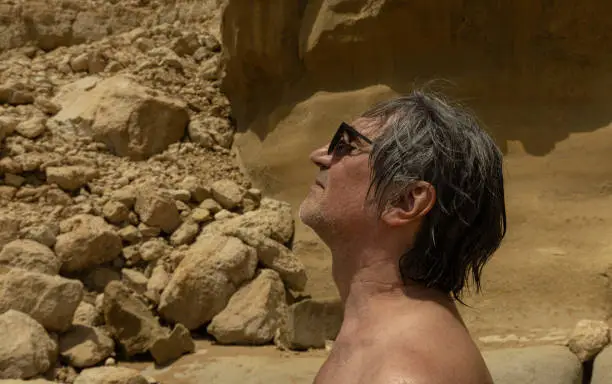 a man sunbathing against the background of textured yellow rock, Crete