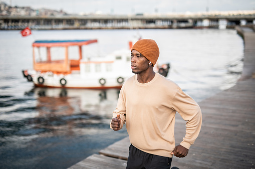 A young black man doing stretching exercises, he is by the sea and enjoys beautiful Istanbul while training outside.