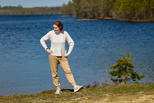 Young woman stands on shore of forest lake in springtime, northern Europe.
