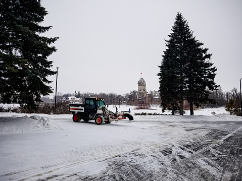 The snow removal vehicle / plow is blowing the snow off of the path at the assiniboine park